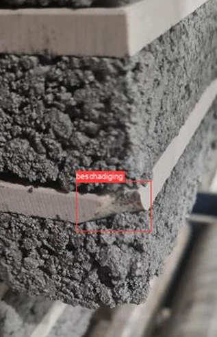 Close-up van gestapelde betontegels. Een afgebroken hoek is met een rood kader gemarkeerd als beschadiging.